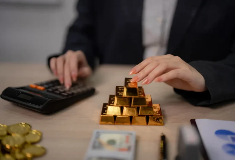 Person calculating income with gold bars and money on a desk