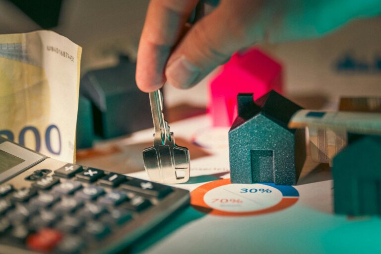 Hand holding a house key near miniature house models, a calculator, and financial charts, symbolizing calculating potential savings with an offset account.