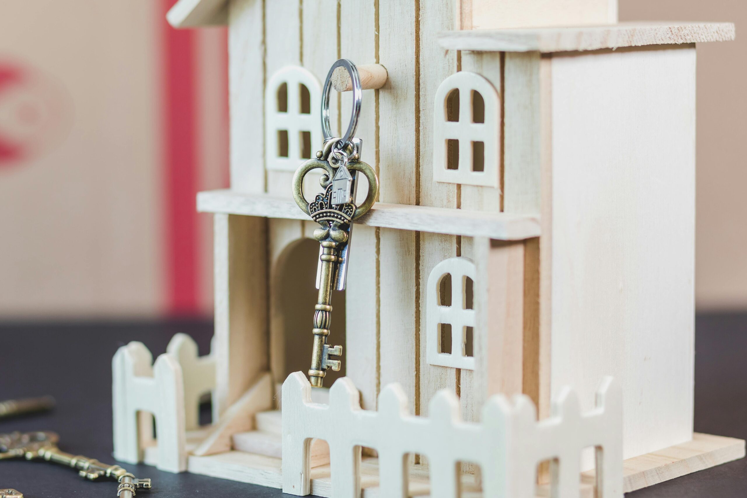 Key with a house-shaped keychain hanging on a wooden model house, symbolizing homeownership and mortgage management.