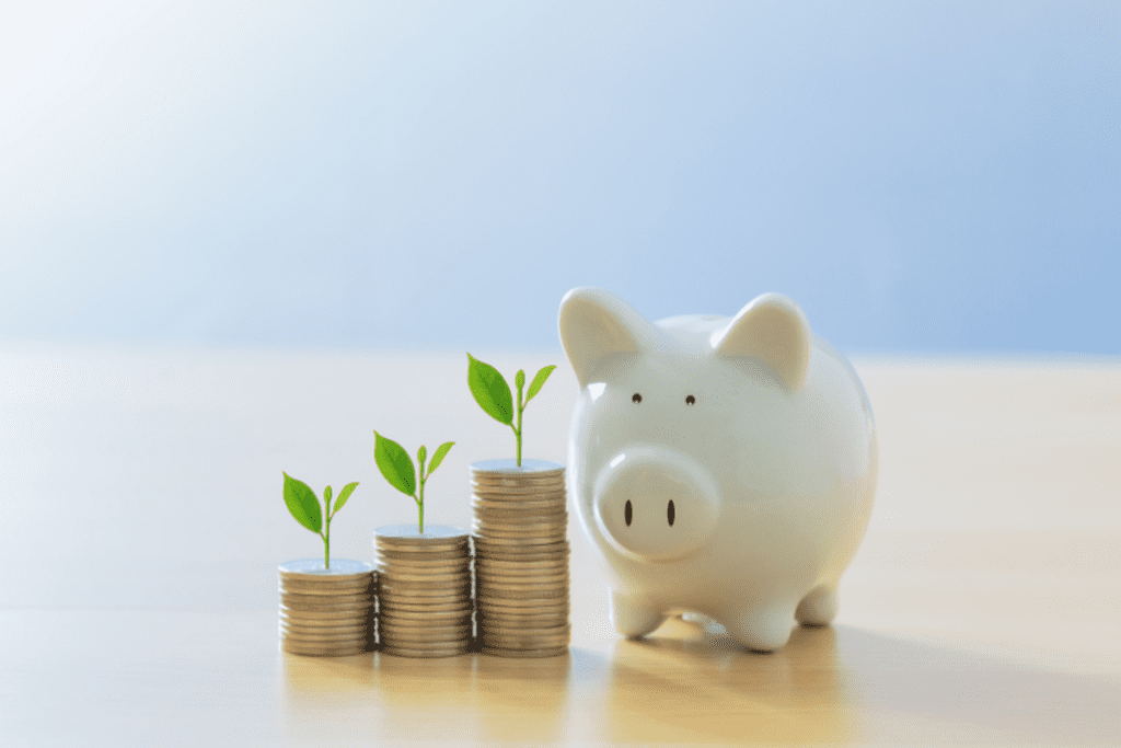 Piggy bank next to stacks of coins with green seedlings growing on top