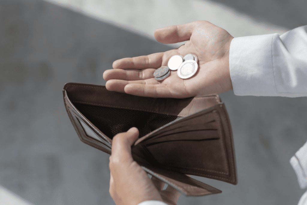 Person holding coins in one hand and an empty wallet in the other