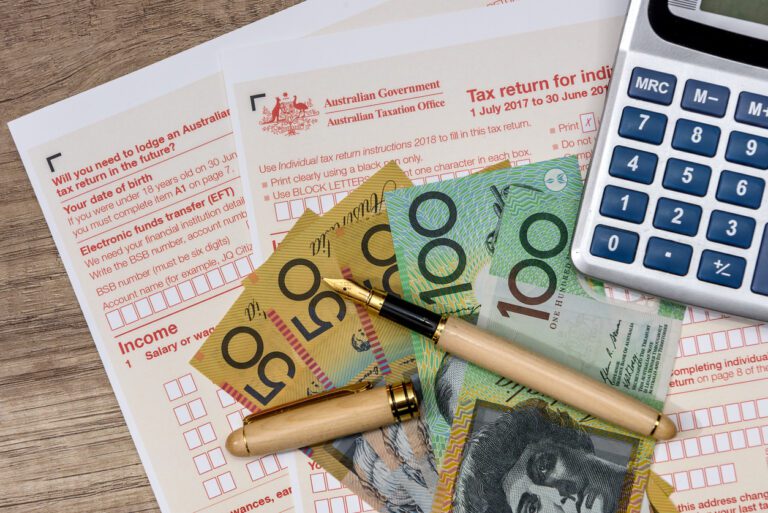 Australian tax return forms with cash, a fountain pen, and a calculator, representing tax planning and financial management.