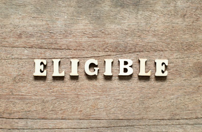 The word “ELIGIBLE” spelled out in wooden blocks on a rustic wooden background.