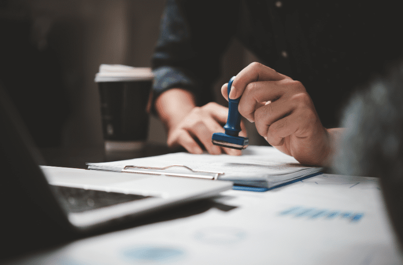 Person stamping a loan document at a desk with laptop and paperwork.
