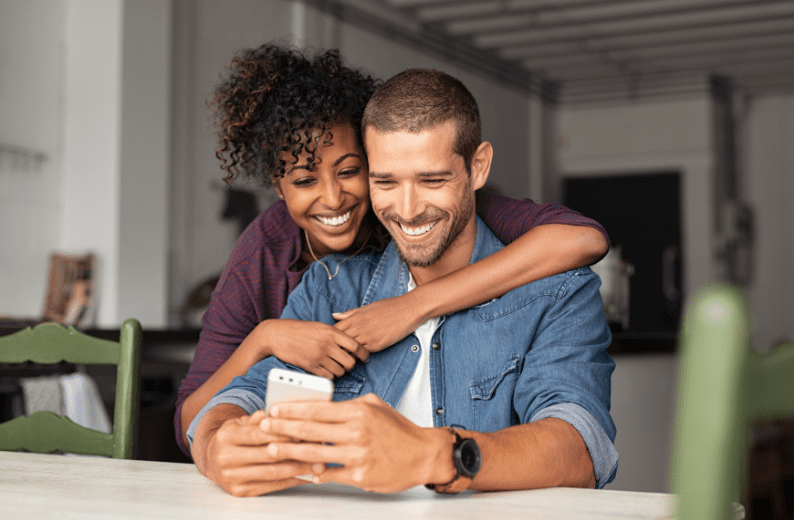 Happy young couple looking at a smartphone together, symbolising first home buyers planning their purchase.