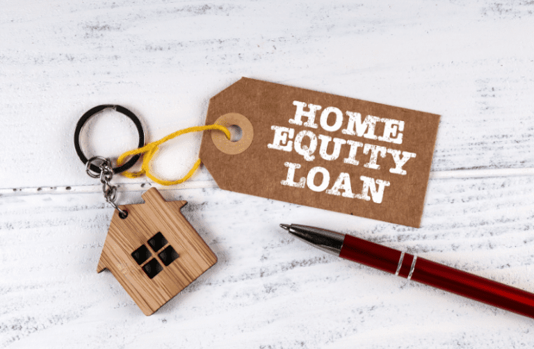 A house-shaped keychain, red pen, and brown label with the words “Home Equity Loan” on a white wooden surface—symbolising the concept of accessing home equity.