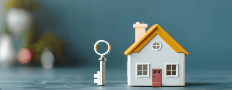 A silver key standing next to a miniature white house with a yellow roof on a dark surface, symbolising unlocking home equity.