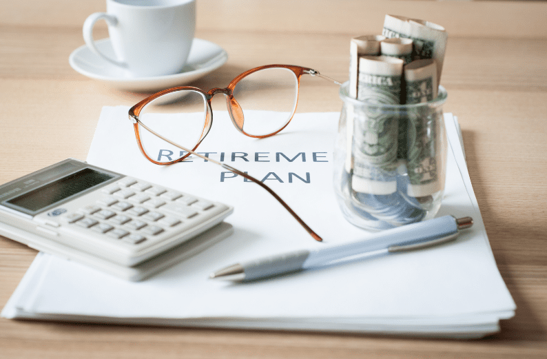 Retirement planning documents with calculator, glasses, and savings jar.