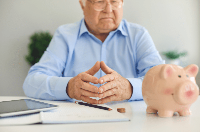 Retiree planning finances with a piggy bank and tablet on table.
