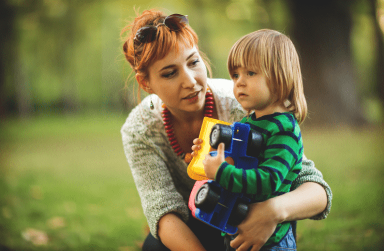Single mother outdoors with her child holding a toy truck.