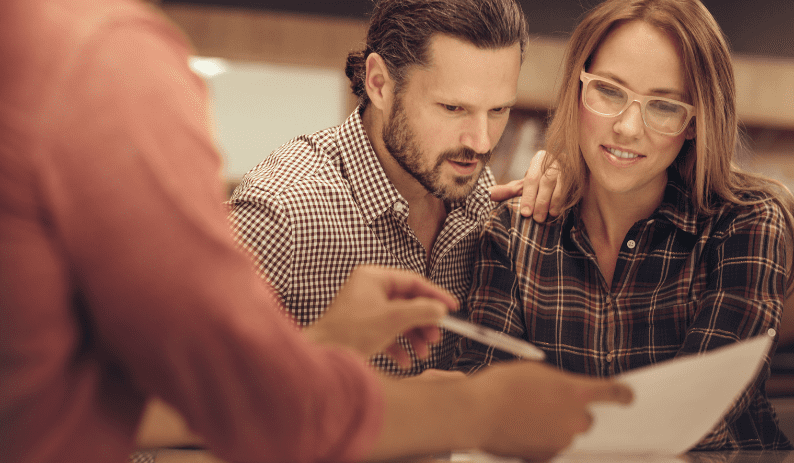 A couple attentively reviewing paperwork with a financial adviser, symbolising the process of applying for a home equity loan.