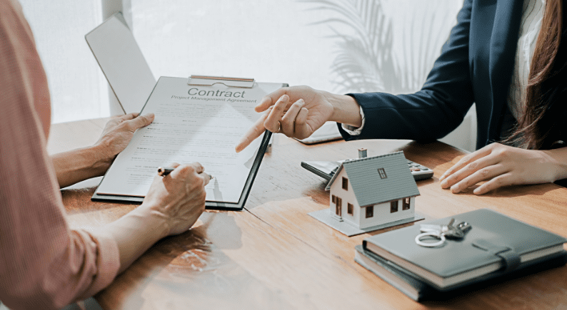 Client signing a home loan contract at a desk with a miniature house and keys.