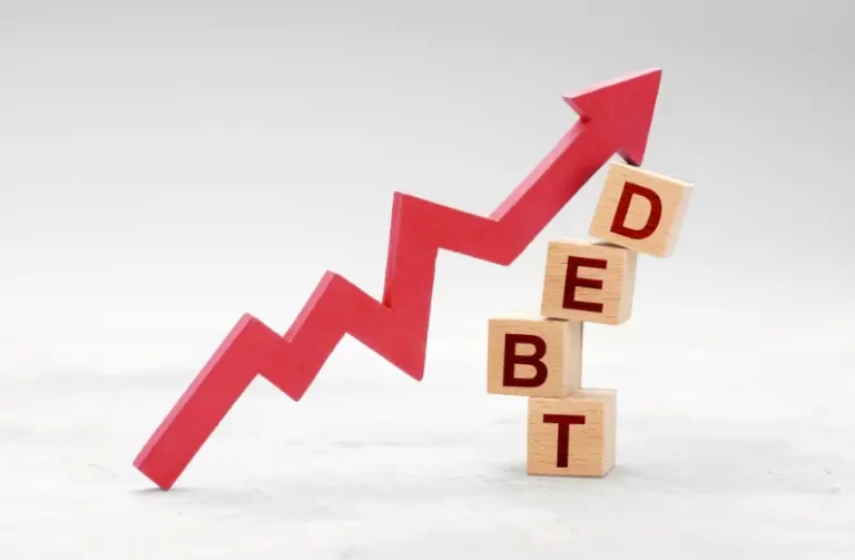 Stacked wooden blocks spelling “DEBT” with a red arrow pointing upward, symbolising growing debt levels.