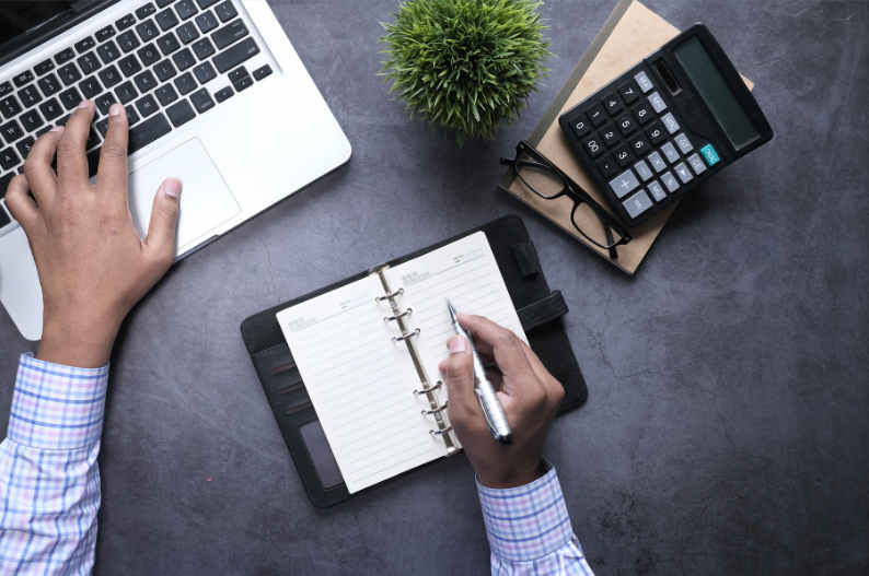 Person planning finances with laptop, notebook and calculator