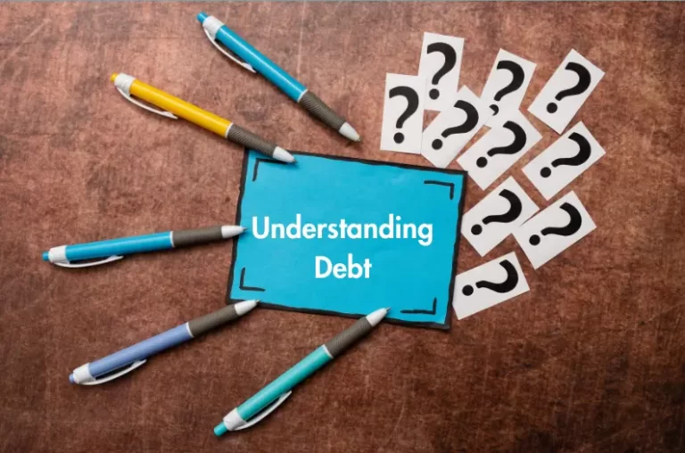 Pens pointing toward a blue card labeled “Understanding Debt,” surrounded by question marks on a brown surface.