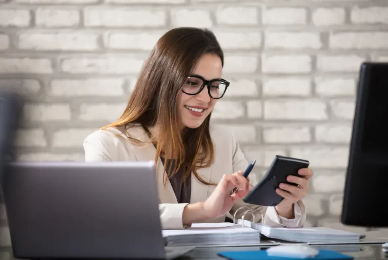 Smiling woman using calculator at desk reviewing her tax return