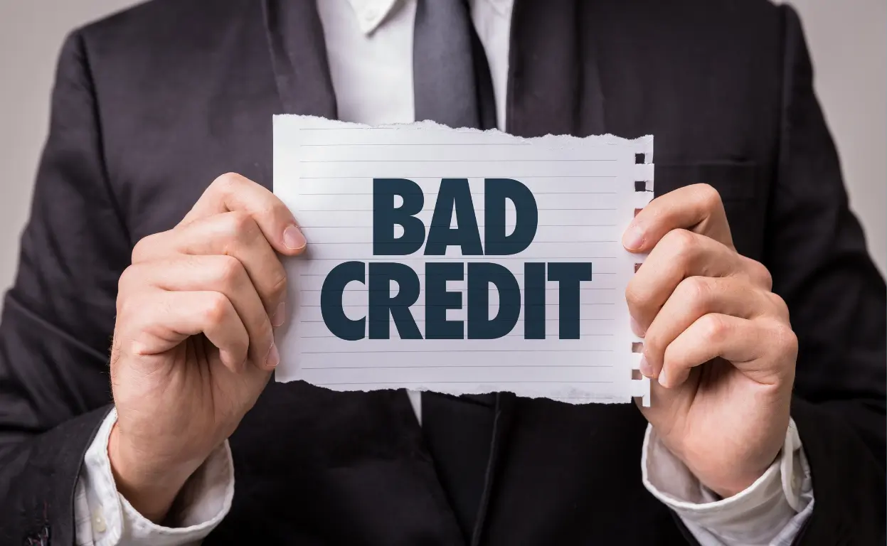 Man in suit holding a sign that says "Bad Credit" – representing poor credit car loan eligibility.