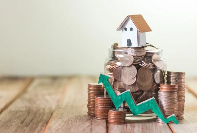 Small house model sitting atop a jar filled with coins, surrounded by stacked coins and a green upward arrow, symbolising property investment growth.