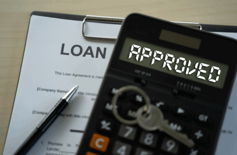 Calculator displaying ‘Approved’ on top of a home loan agreement with house keys.