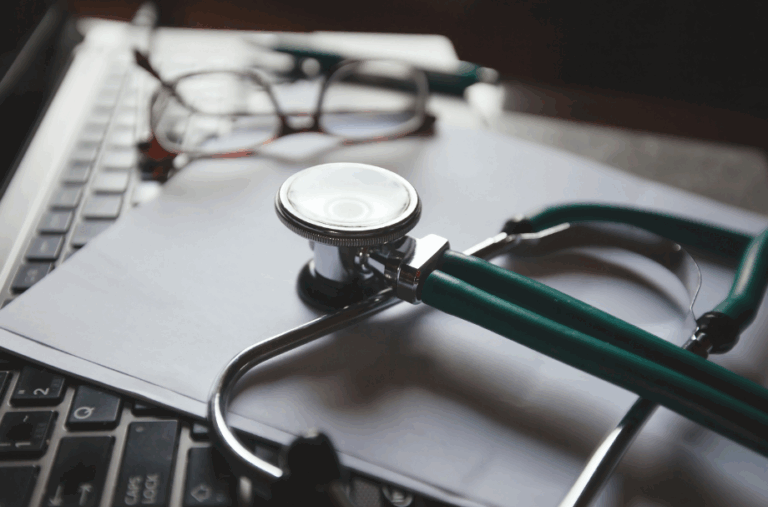 Stethoscope and eyeglasses placed on top of a laptop and paperwork.