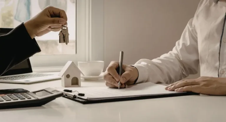 Person signing home loan documents while receiving a set of house keys.