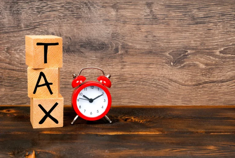 Wooden blocks spelling 'TAX' beside a red alarm clock symbolising Australian tax time and deadlines.